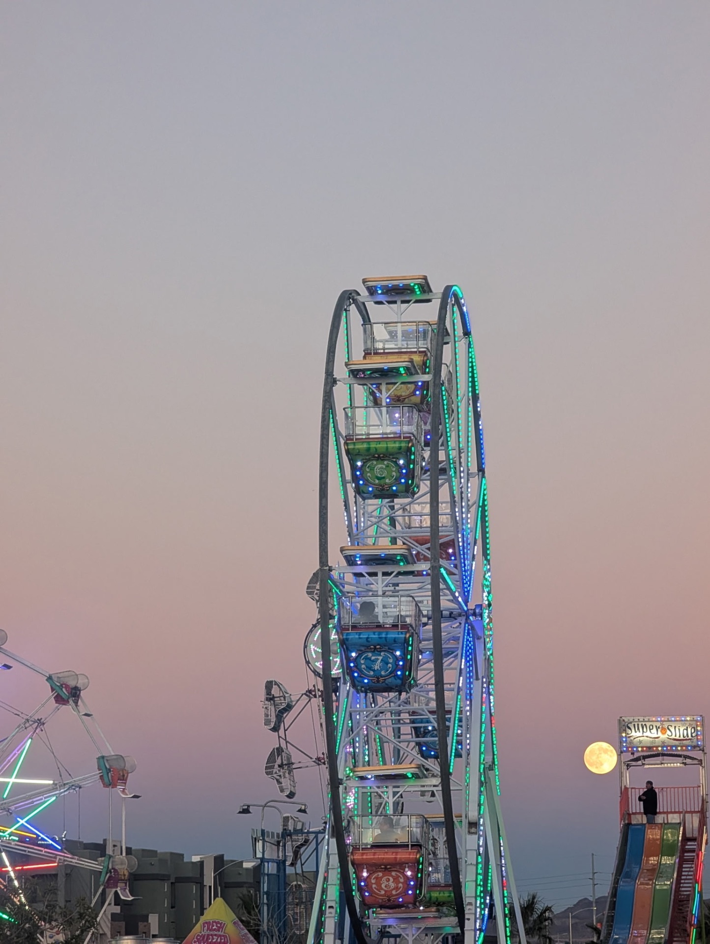Brightly lit Paradise Amusements and Attractions Ferris wheel glowing over the midway at night
