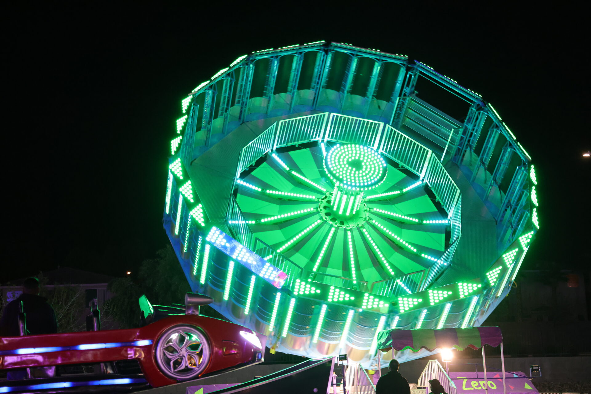 Battech Zero Gravity ride glowing bright green while tilted high above the midway
